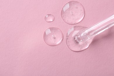 Dripping cosmetic serum from pipette onto pink background, top view. Space for text