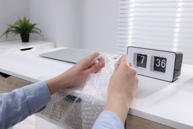 Photo of Woman popping bubble wrap at table in office, closeup. Stress relief