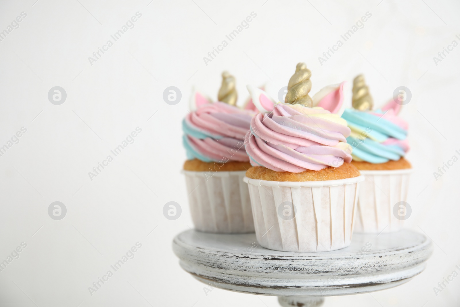 Photo of Cute sweet unicorn cupcakes on dessert stand against   white background. Space for text