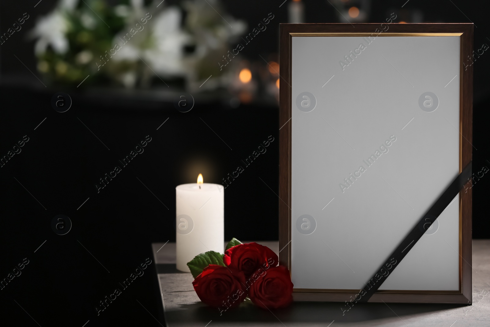 Photo of Funeral photo frame with black ribbon, roses and burning candle on table in dark room