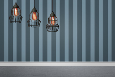 Stylish pendant lamps hanging near striped wall in room