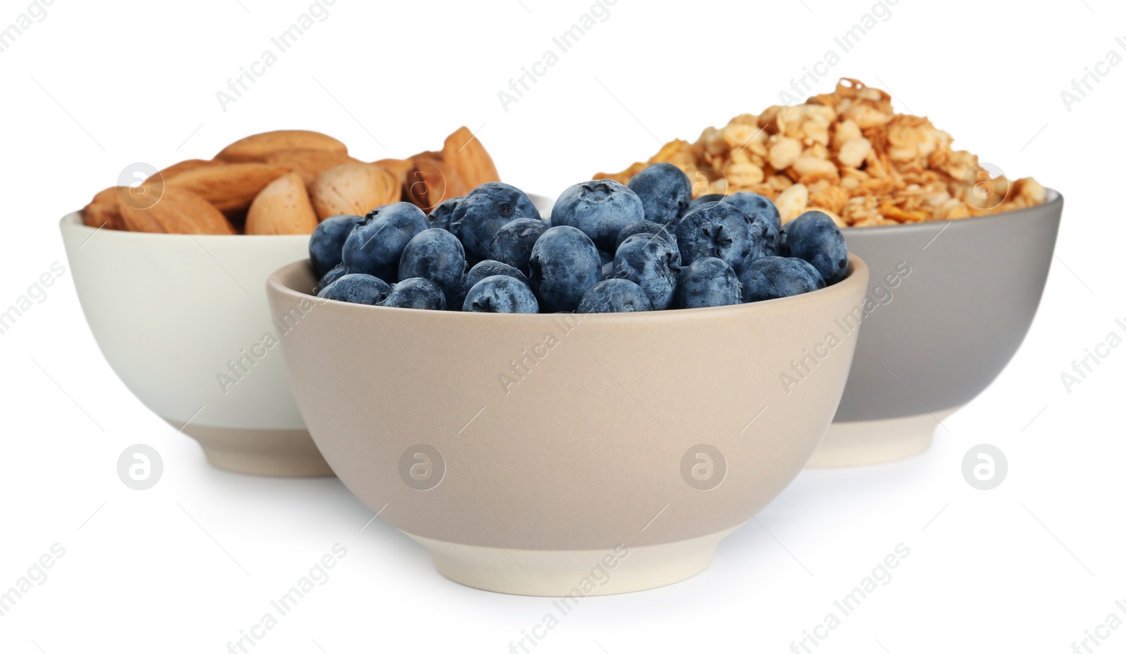 Photo of Ceramic bowls with almonds, blueberries and granola on white background. Cooking utensil