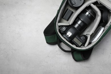Photo of Professional photography equipment in backpack on grey stone table, top view. Space for text
