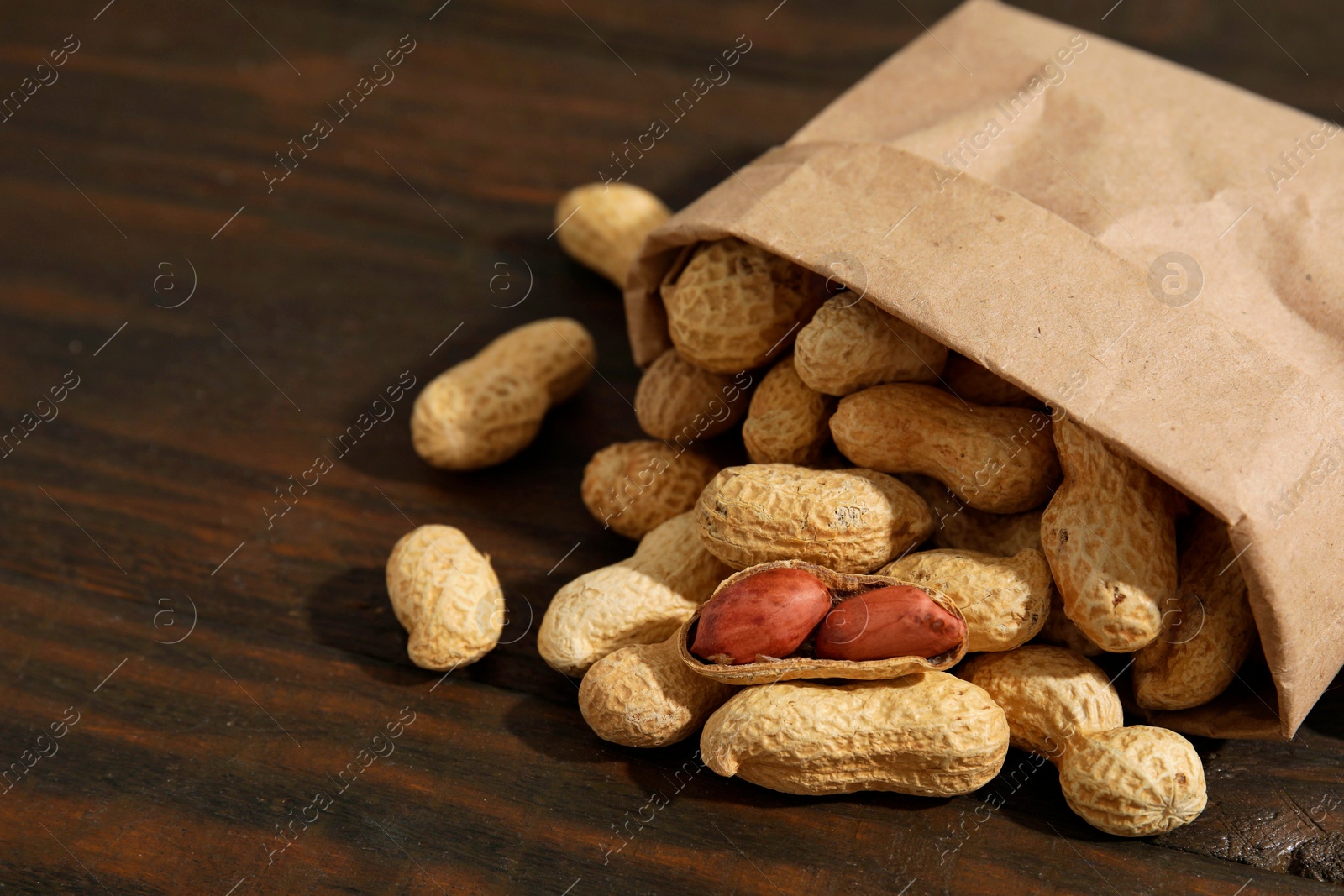 Photo of Paper bag with fresh unpeeled peanuts on wooden table, closeup. Space for text