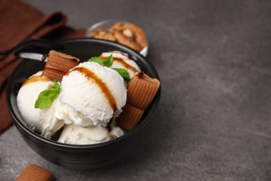 Photo of Bowl of tasty ice cream with caramel sauce, candies and mint on brown table, closeup. Space for text