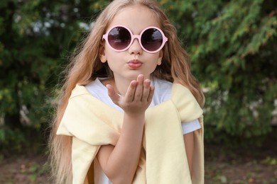 Girl in stylish sunglasses near spruce trees outdoors