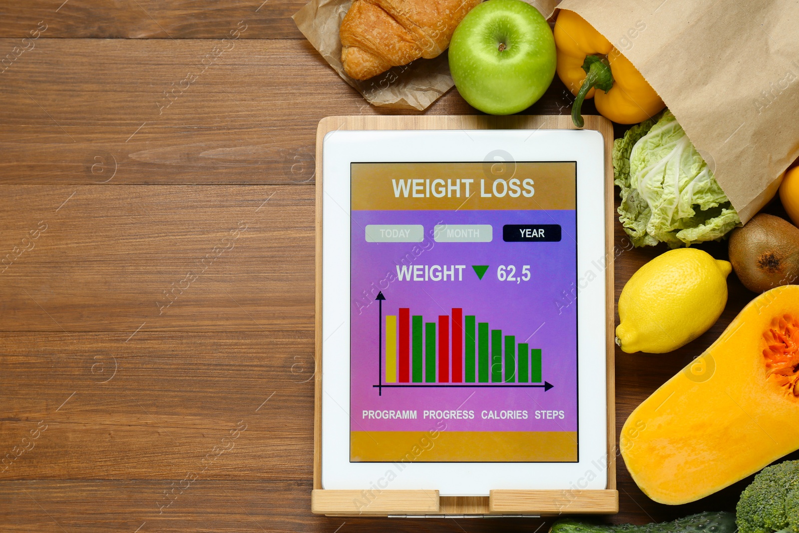 Photo of Tablet with weight loss calculator application and food products on wooden table, flat lay. Space for text