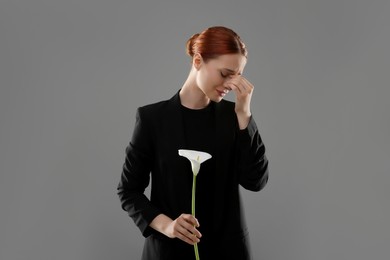 Sad woman with calla lily flower mourning on grey background. Funeral ceremony