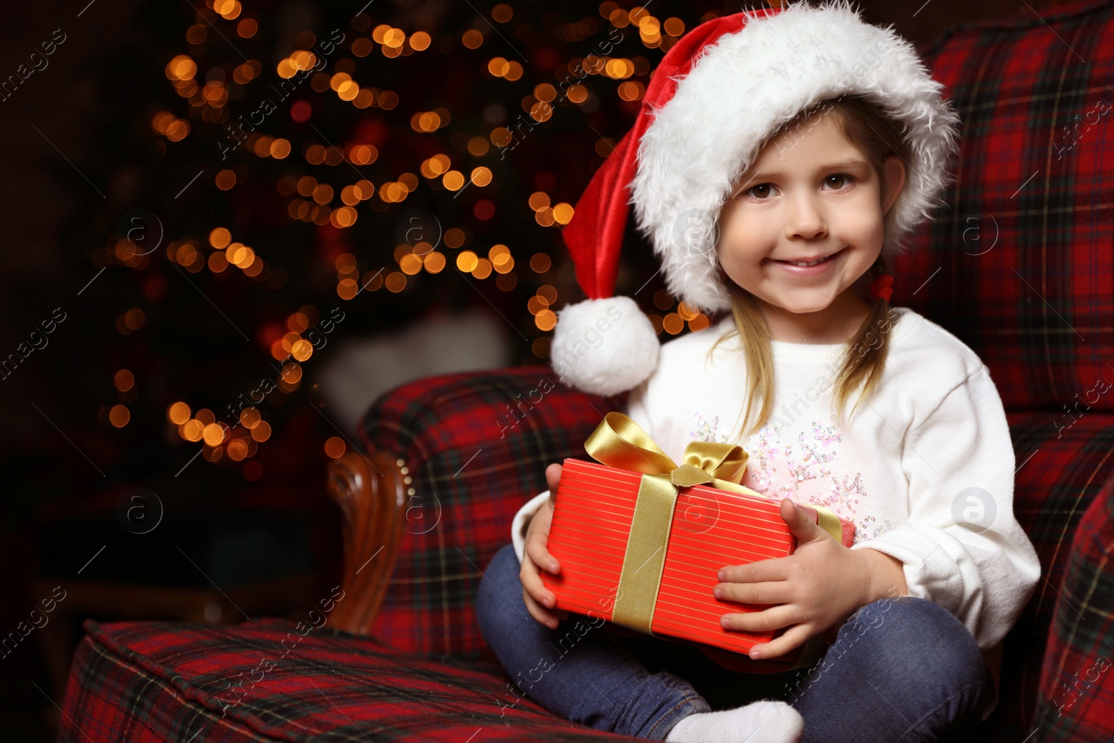 Photo of Cute little child with Christmas gift sitting in armchair at home