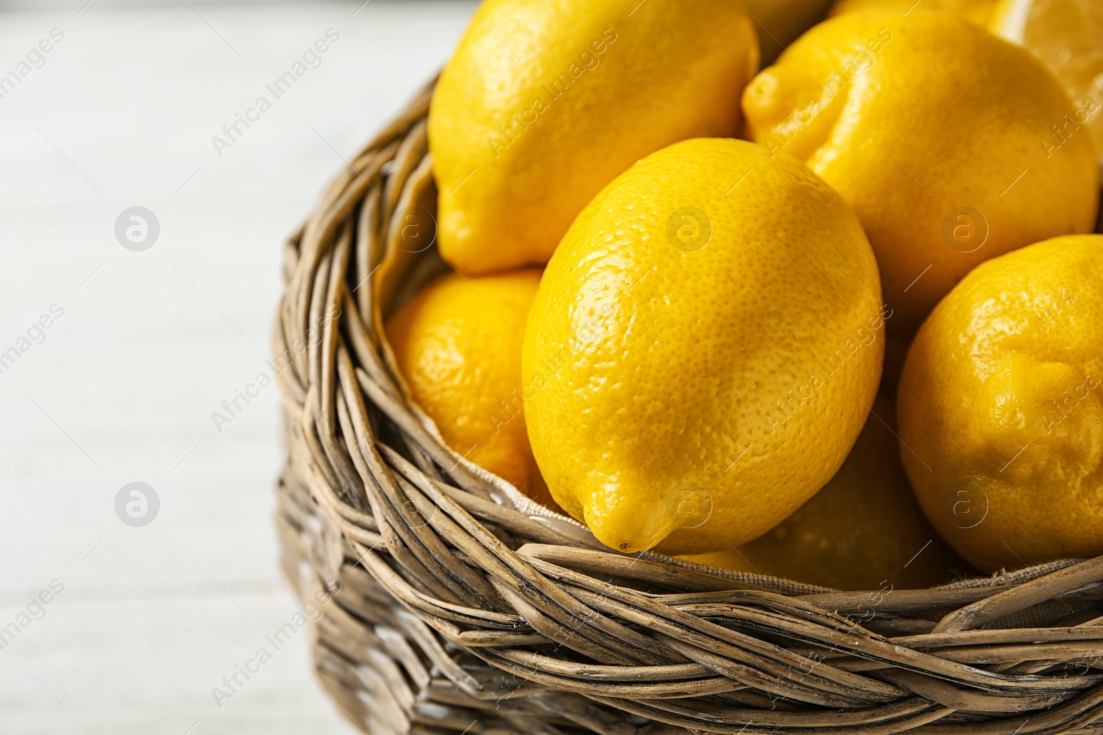 Photo of Basket with ripe lemons on wooden background, closeup