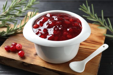 Cranberry sauce in bowl, fresh berries, spoon and rosemary on table, closeup