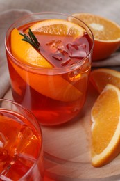Aperol spritz cocktail, ice cubes, rosemary and orange slices in glass on table, closeup