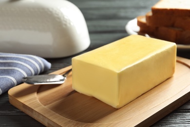 Wooden board with fresh butter and knife on table, closeup