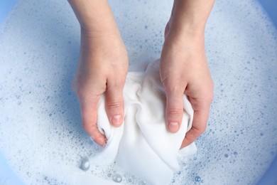 Top view of woman hand washing white clothing in suds, closeup