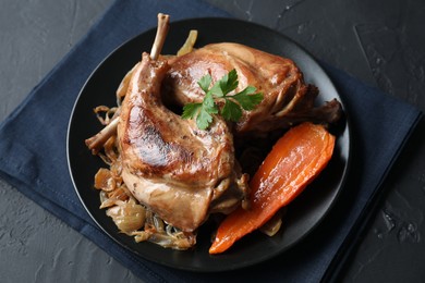 Tasty cooked rabbit meat with vegetables and parsley on black table, above view