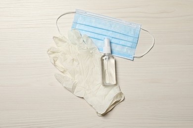 Photo of Medical gloves, mask and hand sanitizer on wooden background, flat lay. Safety equipment