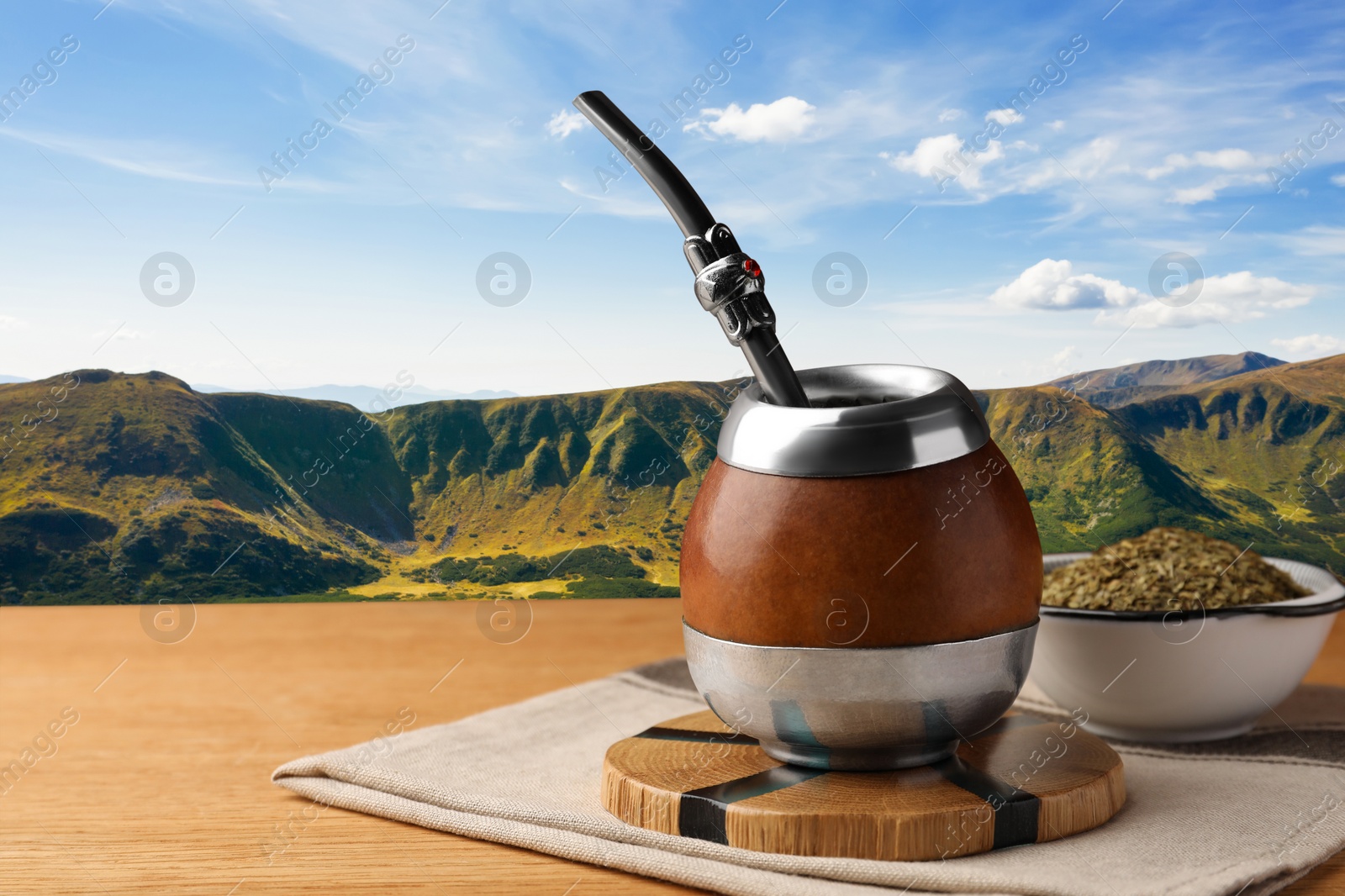 Image of Calabash with mate tea and bombilla on wooden table and beautiful view of mountain landscape, space for text