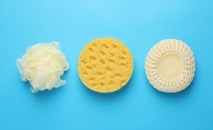 Different sponges on light blue background, flat lay