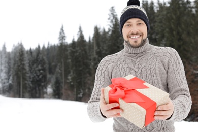 Happy man with gift box outdoors, space for text. Winter vacation