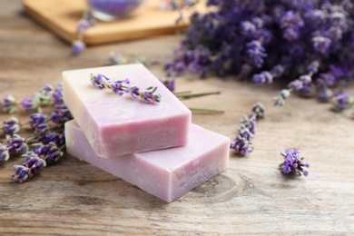 Photo of Handmade soap bars with lavender flowers on brown wooden table, closeup. Space for text