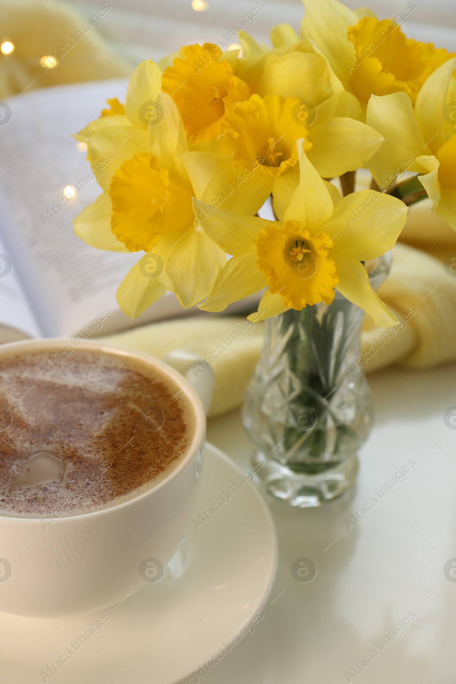 Photo of Beautiful yellow daffodils in vase and cup of coffee on windowsill, closeup