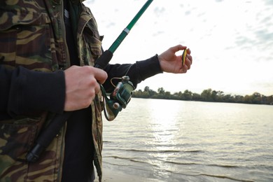 Photo of Fisherman holding fishing rod and lure at riverside, closeup. Space for text