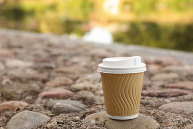 Photo of Paper cup on rocky ground outdoors, space for text. Coffee to go