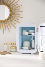 Photo of Cosmetics refrigerator and skin care products on white vanity table indoors