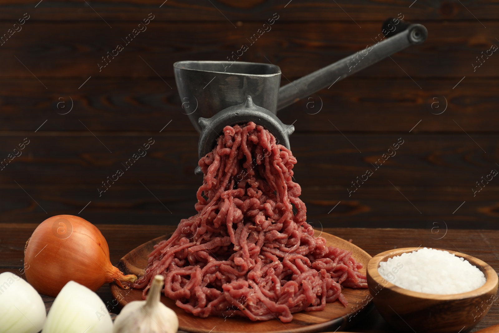 Photo of Meat grinder with beef mince, onion, garlic and salt on wooden table