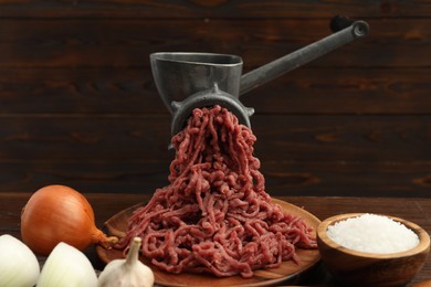 Meat grinder with beef mince, onion, garlic and salt on wooden table