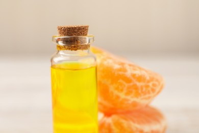 Bottle of tangerine essential oil and fresh fruit on table, closeup