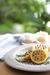 Photo of Lemons with cloves and fresh rosemary on wooden table outdoors, closeup. Natural homemade repellent