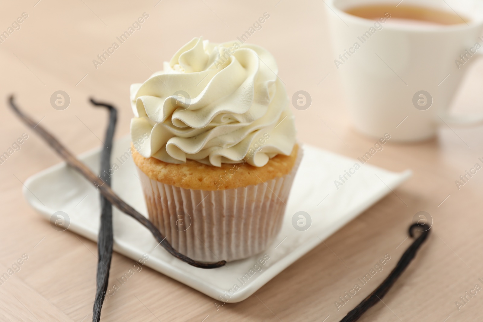 Photo of Tasty cupcake with cream and vanilla pods on light wooden table, closeup