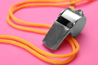 One metal whistle with cord on pink background, closeup