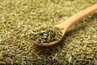 Heap of fennel seeds and wooden spoon as background, closeup