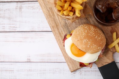 Photo of Delicious burger with fried egg, french fries and soda drink served on white wooden table, flat lay. Space for text