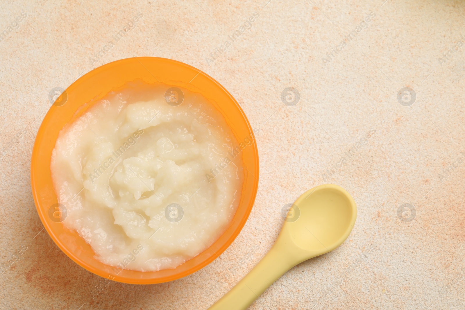 Photo of Baby food. Bowl with cauliflower puree served on beige textured table, flat lay