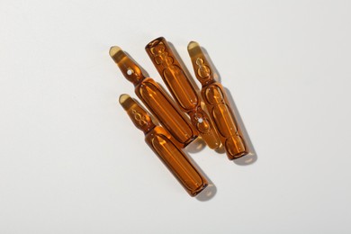 Glass ampoules with liquid on white background, top view