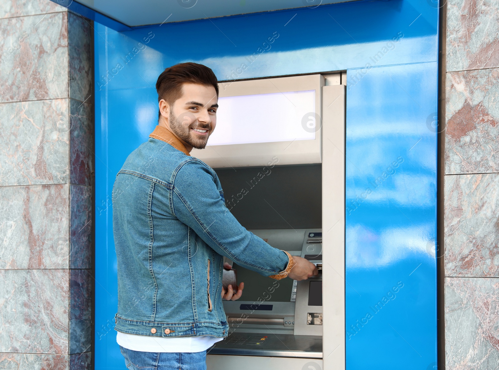 Photo of Young man using modern cash machine outdoors