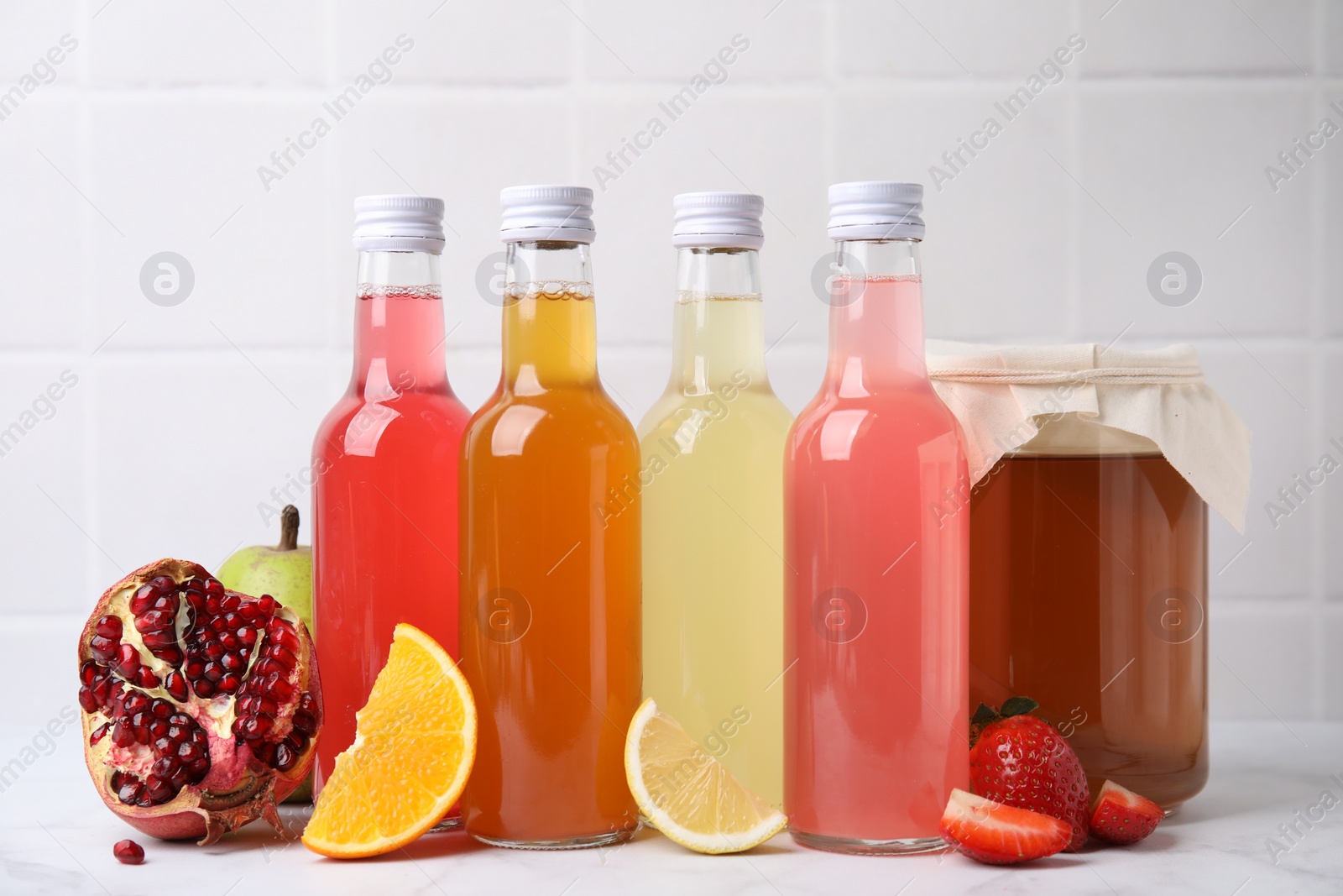 Photo of Delicious kombucha in glass bottles, jar and fresh fruits on white marble table