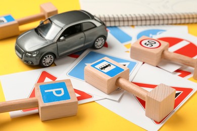 Photo of Many different road signs and toy car on yellow background, closeup. Driving school
