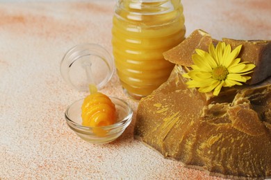 Photo of Natural beeswax blocks, flower and jar of honey on color textured table, closeup. Space for text