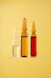 Photo of Glass ampoules with liquid on yellow background