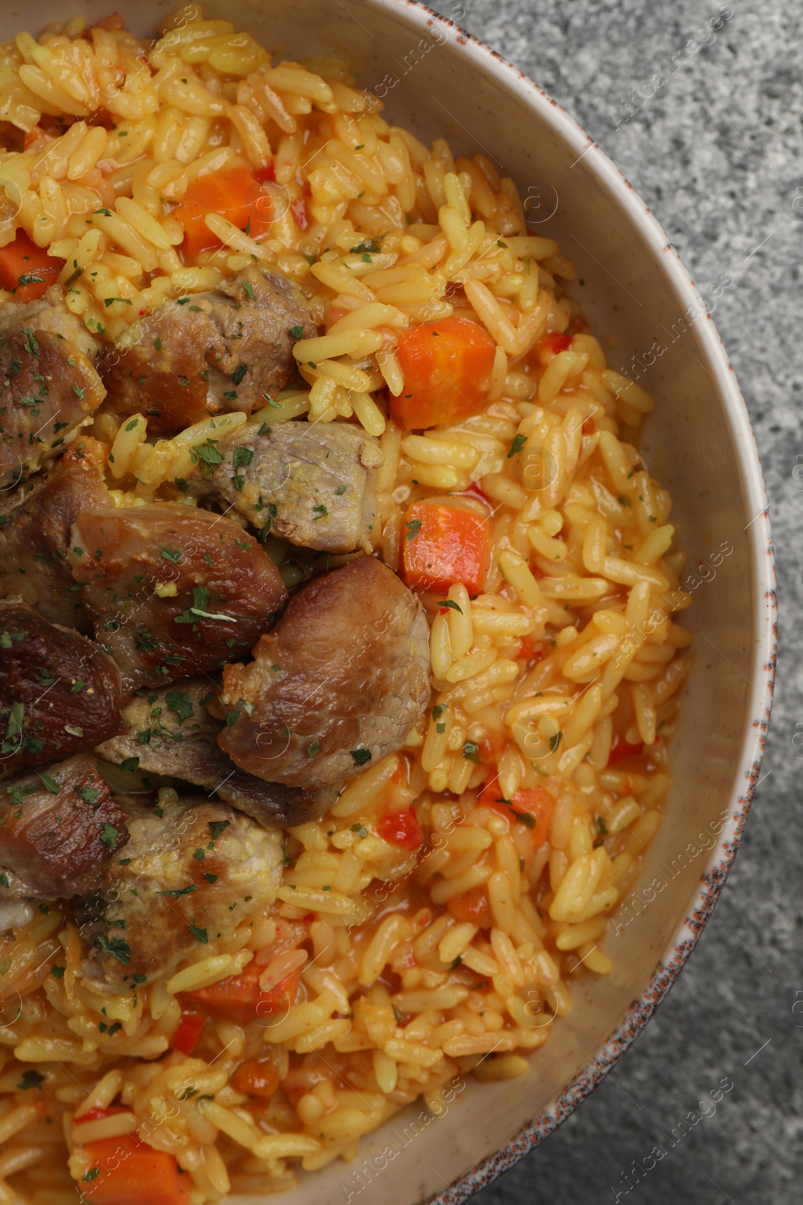 Photo of Delicious pilaf with meat on grey textured table, top view