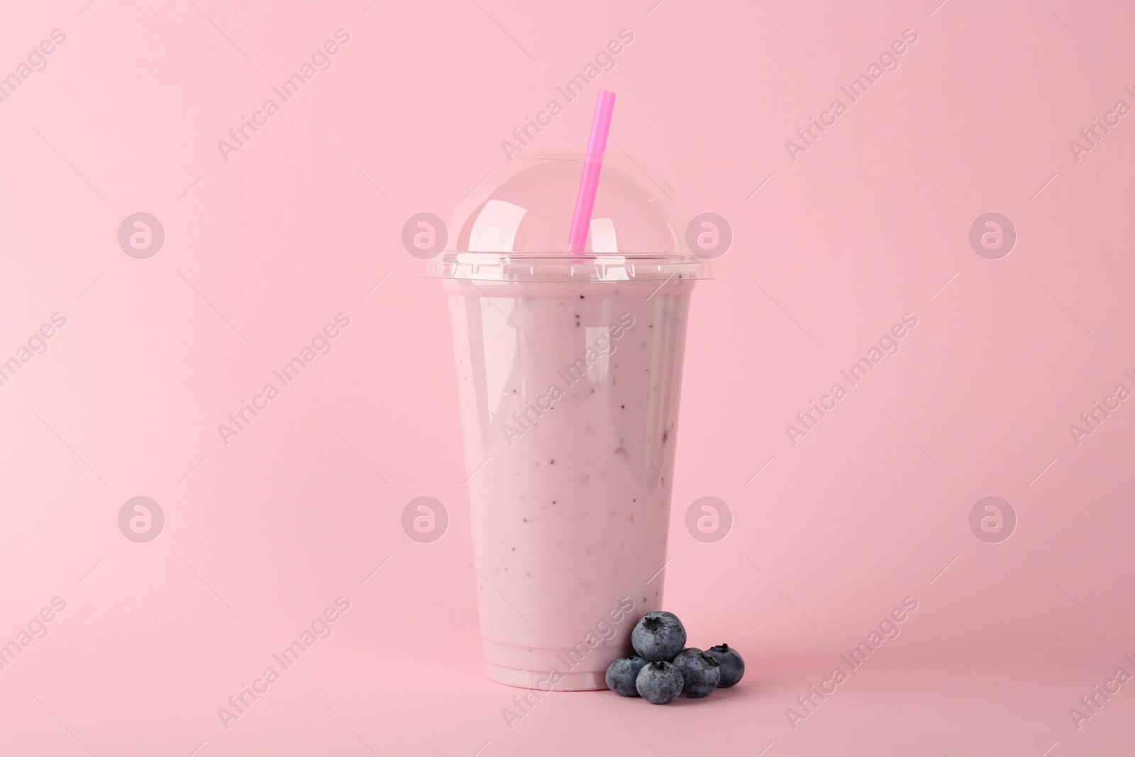 Photo of Plastic cup of tasty smoothie and fresh blueberries on pink background