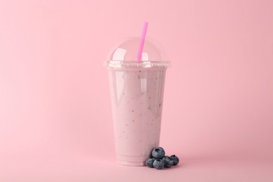 Plastic cup of tasty smoothie and fresh blueberries on pink background