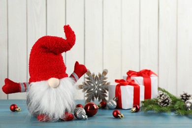 Photo of Cute Christmas gnome, gift boxes and festive decor on turquoise table against white wooden background