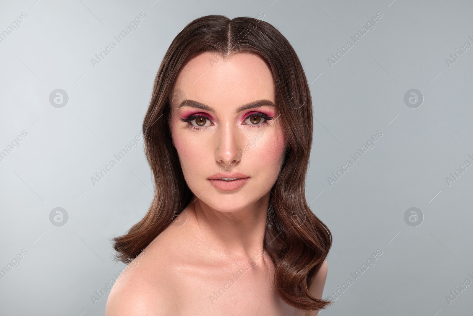 Photo of Portrait of beautiful young woman with makeup and gorgeous hair styling on light grey background