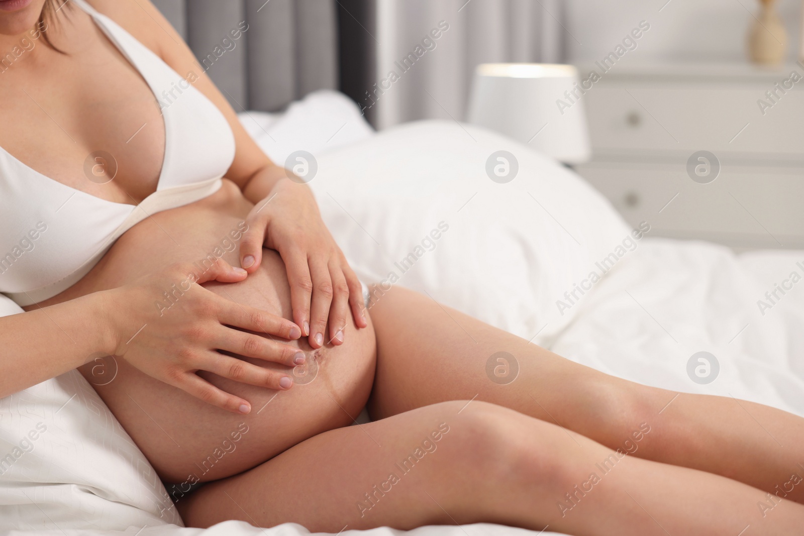 Photo of Pregnant woman in stylish comfortable underwear making heart with hands on her belly in bedroom, closeup