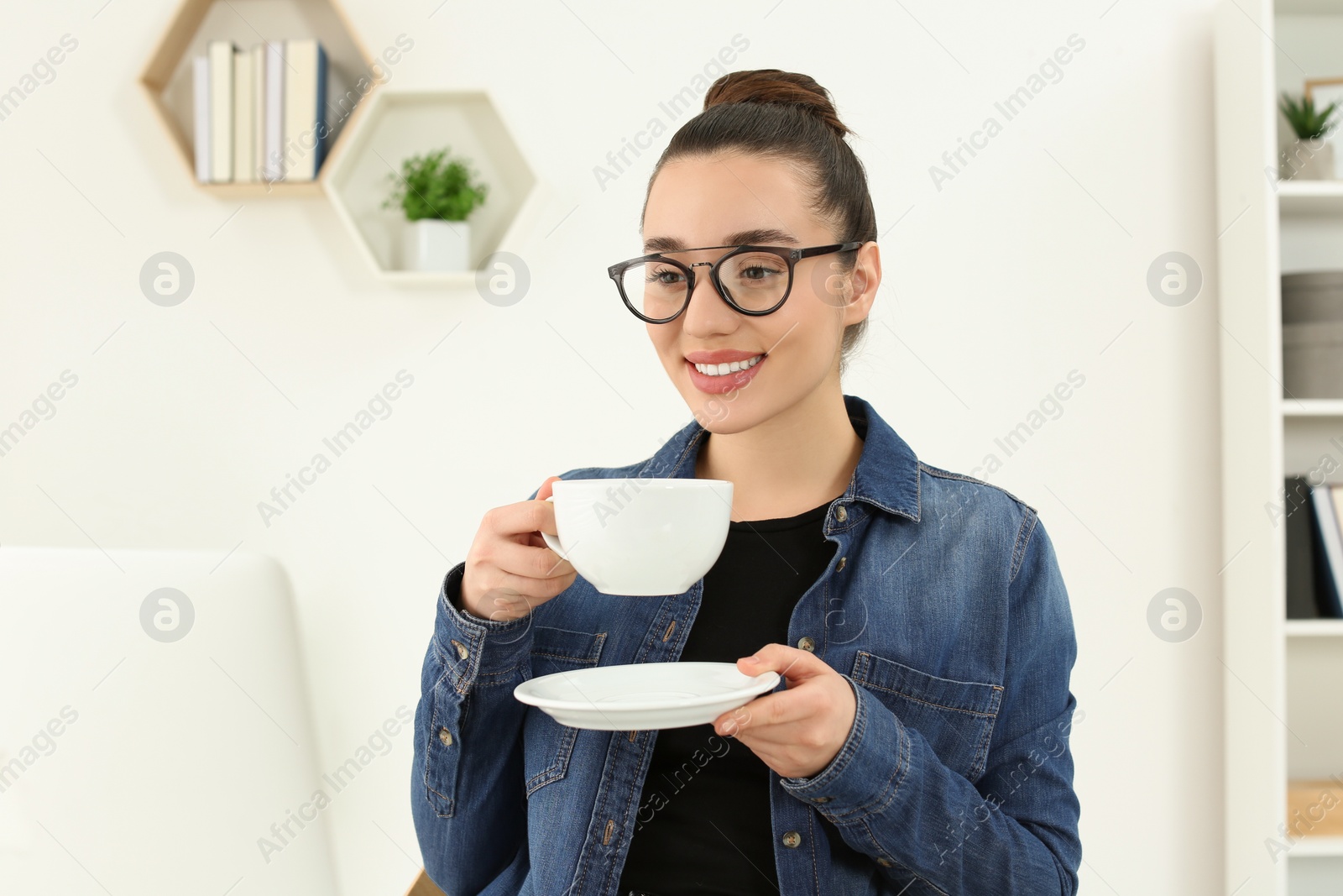 Photo of Home workplace. Happy woman with cup of hot drink looking at laptop in room